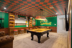 Welcome to a lively game room with a classic billiards table and playful "The Simpsons" decor. Enjoy the fun red and green checkerboard ceiling, cozy seating, and a stylish bar area for a perfect spot to relax and have fun.