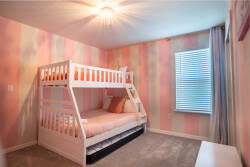 This charming bedroom is bright and playful, featuring a cozy bunk bed with crisp white framing that's perfect for kids or guests. Soft pink striped walls and natural light create a cheerful and inviting atmosphere.