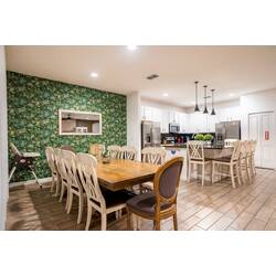Gather in a bright open kitchen and dining area with white cabinets, stainless steel appliances, black countertops, and island seating. Pendant lights, wood-look floors, and a large dining table create a welcoming space for family meals.
