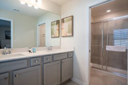 This bright bathroom features a spacious double vanity with sleek gray cabinetry and elegant fixtures. Enjoy stylish artwork that adds personality, and indulge in a refreshing experience in the modern glass-enclosed shower.