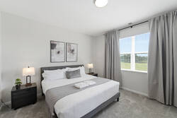 Rest in a bright and cozy bedroom with a comfortable bed, soft gray accents, bedside lamps, wall art, large window, carpeted flooring, and peaceful green views for a relaxing stay.