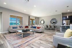 Sunlight fills this spacious living area, showcasing soft gray sofas with colorful pillows and a chic rug. With inviting mirrors and a smooth transition to the dining area, it’s an ideal spot for relaxation and socializing.
