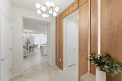 English, US:
Welcome guests through a bright entry hall with warm wood panels, mirror accents, modern globe chandelier, soft neutral tones, tile flooring, and a view toward the open dining and kitchen areas.