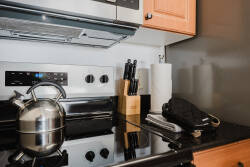 This kitchen corner features sleek black countertops and warm wooden cabinetry, offering a stylish and functional space. A polished stainless steel kettle and neatly arranged knives invite you to embark on culinary adventures.
