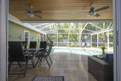Step into this sunlit space where sleek ceiling fans circulate warm breezes above a stylish dining area. The polished tile flooring complements the tranquil pool view, inviting you to unwind in this charming indoor-outdoor oasis.