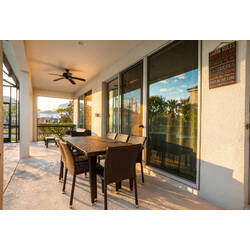 Enjoy a covered lanai with a wicker dining table, ceiling fan, and large sliding doors reflecting the pool area. Warm sunlight, outdoor seating, and peaceful views create a cozy spot for meals and relaxing Florida evenings.