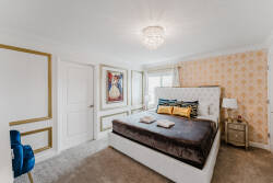 Experience a beautifully designed bedroom featuring a plush bed with rich bedding and luxurious pillows. The soft carpet, elegant gold-framed artwork, and stylish light fixture create a cozy, chic atmosphere just for you.