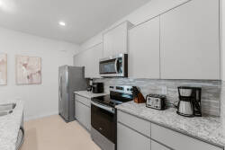 Welcome to this elegant kitchen with sleek gray cabinetry and a chic granite countertop, perfect for cooking. Enjoy stainless steel appliances, including a microwave and coffee maker, in this warm space with soft ambient lighting.