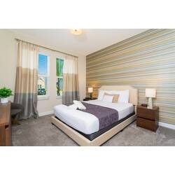 Rest in a bright bedroom with a comfortable bed, soft white bedding, striped accent wall, neutral curtains, bedside lamps, carpeted floor, and warm modern decor.