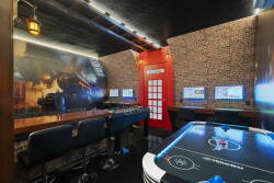 Enjoy a vibrant game room featuring a sleek air hockey table and interactive screens, all highlighted by a beautiful exposed brick wall. The charming red phone booth adds a delightful touch for fun with friends and family.