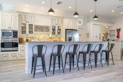 Welcome to our beautifully designed kitchen, complete with a spacious island featuring a sleek gray countertop and stylish black metal bar stools.