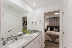 Experience a bright, modern bathroom with stylish dual sinks on a polished granite countertop and warm, neutral tones. Just beyond, a cozy bedroom awaits for restful nights after your adventures.