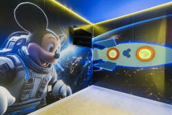 Enter a lively playroom featuring a cheerful astronaut Mickey Mouse and a colorful rocket on the walls, sparking imagination and adventure. The vibrant blue tones and gentle lighting create an inviting space for young explorers.
