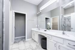 Step into a sleek bathroom featuring a spacious dual vanity topped with polished white countertops, surrounded by modern gray walls. The elegant marble floor adds a touch of luxury, creating a refreshing atmosphere for your stay.