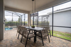 Step onto the charming screened-in patio, featuring a stylish wooden dining table perfect for outdoor meals. With warm paver flooring and cozy seating, it’s an inviting space to relax by the sparkling pool.