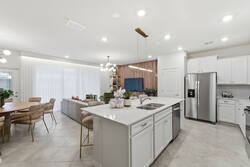Cook with ease in a bright modern kitchen with white cabinets, stainless steel appliances, spacious counters, a large island, soft lighting, and an open view to the living room, perfect for family meals during vacation.
