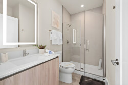 Experience a beautifully designed bathroom with a sleek glass shower and warm wood cabinetry for a calming atmosphere. The bright, backlit mirror adds modern sophistication, enhancing the pleasure of your daily routine.