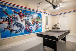 Have fun in a superhero themed game garage with a ping pong table, bold wall art, ceiling fan, and open space, creating a fun spot for family entertainment during vacation.