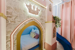 Immerse yourself in a whimsical castle-themed retreat, where a cozy bed with soft cushions and a playful slide await. The enchanting pink hues and glowing crown detail set the stage for delightful imaginative adventures.