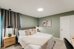 Experience a bright and cozy bedroom with a plush queen bed dressed in soft linens and decorative pillows, surrounded by calming green walls. Stylish lamps and modern artwork enhance the inviting atmosphere for your relaxation.
