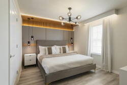 Wake up refreshed in this cozy bedroom featuring a plush king-sized bed, warm wood accents, and stylish sconces. Natural light pours in, creating a modern atmosphere that's perfect for your relaxation and comfort.