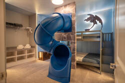 This playful room features a vibrant blue slide and a cozy bunk bed, creating a whimsical atmosphere for kids. With soft gray carpeting and cheerful wall art, it promises inviting and fun-filled nights for your little ones.