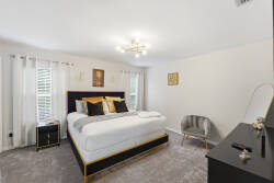 Experience a cozy retreat in this stylish bedroom featuring a plush king-sized bed with elegant black and gold accents. Let the natural light brighten the inviting space, complemented by soft carpet and modern lighting for your.