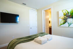 This cozy bedroom features a plush bed adorned with a soft green throw, inviting relaxation after a day of adventure. A vibrant floral artwork adds a splash of color, while the mounted TV ensures entertainment at your fingertips.