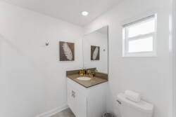 Bright and airy, this bathroom features a chic minimalist design with a spacious vanity topped in rich brown, complemented by sleek gold fixtures. Natural light spills in through a window, enhancing the fresh, clean aesthetic.