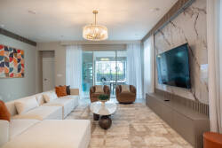 Enter a bright living room featuring a stunning marble accent wall and a sleek chandelier. The plush white sectional and cozy brown armchairs offer a stylish yet comfortable space, ideal for unwinding or hosting friends.