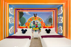 This bright and playful room features two cozy beds with charming Mickey Mouse plushes and vibrant orange and purple accents. The whimsical mural of Mickey Park adds fun, creating a delightful atmosphere for guests of all ages.