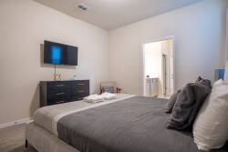 Enjoy a cozy stay in this stylish bedroom, complete with a plush gray bed, soft linens, and a welcoming throw. The minimalist design, flat-screen TV, and warm lighting create the perfect atmosphere for your relaxation.