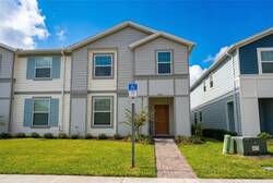 Arrive at a welcoming vacation home with a bright exterior, blue shutters, paved walkway, manicured lawn, and clear blue sky, creating a cheerful first impression for your stay.