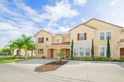 This charming exterior, with its warm yellow façade and classic red shutters, is bathed in natural light. Lush palm trees frame the entrance, inviting you to enjoy a welcoming atmosphere in a beautifully landscaped setting.