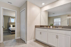 This bright bathroom boasts a sleek double vanity with polished countertops for your morning routine. The soft beige walls enhance the modern fixtures, and a view of the cozy bedroom adds a comforting touch to your stay.