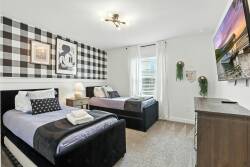 Experience a stylish bedroom with a striking black and white plaid accent wall and cozy twin beds. Natural light floods the room, highlighting the inviting textures of the soft carpet and wooden dresser for a welcoming atmosphere.