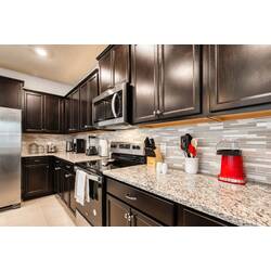 This beautifully designed kitchen features dark cabinetry and sparkling granite countertops, creating a stylish and functional space perfect for effortless meal preparation with modern appliances and a chic backsplash.