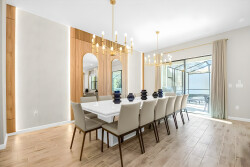 Enjoy stylish dining in this chic space, featuring a sleek white table and contemporary upholstered chairs. Natural light enhances the warm wood accents and elegant chandelier, creating a perfect setting for your gatherings.