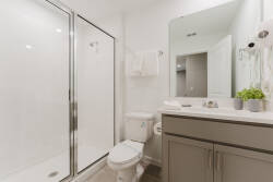 Bright and airy, this bathroom features a spacious glass shower and sleek cabinetry with a subtle gray finish, enhancing its contemporary feel. Fresh towels are neatly arranged, adding a touch of comfort to your stay.