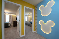 Step into a vibrant hallway where cheerful yellow walls meet playful blue accents, featuring charming illuminated Mickey Mouse silhouettes. The inviting layout seamlessly connects cozy spaces, perfect for a relaxing stay.
