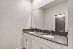 Enjoy this spacious bathroom featuring a double vanity, modern sink fixtures, and a striking dark countertop that complements the white cabinetry. The bright atmosphere creates a refreshing start to your morning routine.