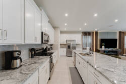 This modern kitchen features glossy white cabinets and spacious granite countertops, creating a bright space for meal prep. Equipped with stainless steel appliances and stylish lighting, it's perfect for your culinary creativity.