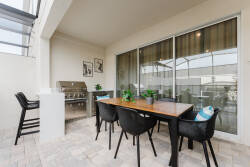 Step outside to this charming patio, where a stylish wooden dining table invites al fresco meals. With sleek black chairs and a backdrop of greenery, it’s an ideal spot to relax or enjoy a barbecue on the grill.
