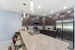 Cook with ease in a bright kitchen with dark cabinets, granite countertops, stainless steel appliances, pendant lights, and bar seating, creating a practical space for meals during your vacation.