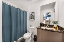 Experience a stylish bathroom with a sleek dark wood vanity and modern fixtures, creating a chic atmosphere. A calming blue shower curtain adds a vibrant touch, while natural light brightens the space for your comfort.