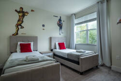 Enhance your stay in this cheerful room with two cozy beds dressed in plush gray linens and vibrant red accents. Fun superhero wall art adds charm, and a large window fills the space with natural light for a bright atmosphere.