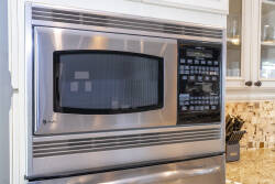 Experience a stylish kitchen with a stainless steel microwave integrated into cabinetry, enhanced by a beautiful mosaic tile backsplash. Enjoy modern appliances in a design that adds warmth and elegance to your space.