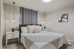 Rest in a modern bedroom with a cozy bed, soft neutral tones, pendant lighting, wall-mounted TV, white console, and simple decor, creating a calm space to relax during vacation.