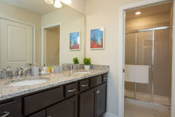 Experience a bright and airy bathroom with a sleek granite countertop that contrasts beautifully with dark cabinetry and vibrant artwork. Enjoy the spacious walk-in shower designed for your comfort and relaxation.