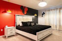 Rest in a Mickey themed bedroom with a cozy bed, bold red and black accent wall, yellow pendant lights, soft curtains, and playful character decor, creating a fun and comfortable space for vacation.